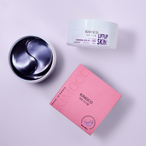 Z lewej otwarty pojemnik z fioletowymi płatkami pod oczy, z prawej zamknięty pojemnik "Kimoco Lift-Up Skin Firming Hydrogel Eye Patches" i różowe pudełko produktu, na jasnofioletowym tle.