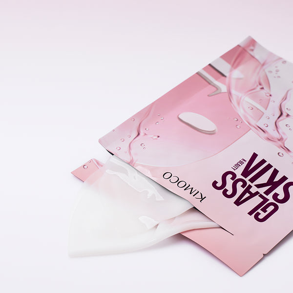Opakowanie "Kimoco Glass Skin" z wysuwającą się z niego złożoną hydrożelową maseczką, na jasnym tle.